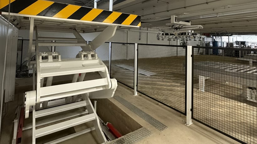 Table élévatrice à ciseaux blanche en installation en fosse : vue dans la fosse en béton ouverte sous la plateforme levée avec marquage de sécurité, clôture de protection à côté
